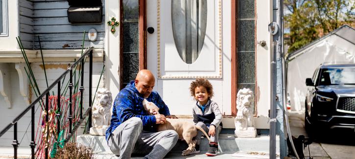 A man and child sit on the front steps of a home with their dog.