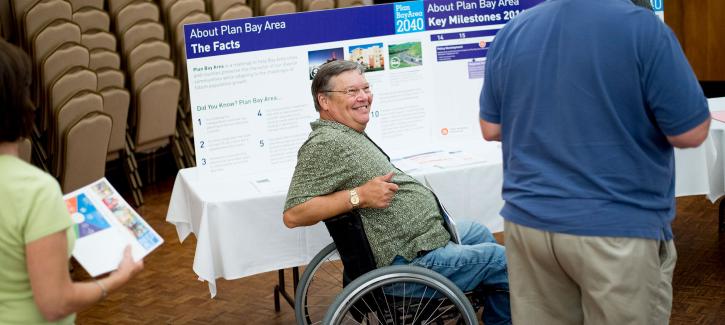 A man in a wheelchair next to a Plan Bay Area 2040 display board.
